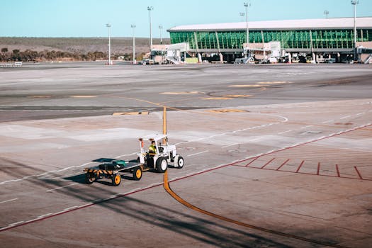 A luggage cart on the airport tarmac near a modern terminal building under clear skies.