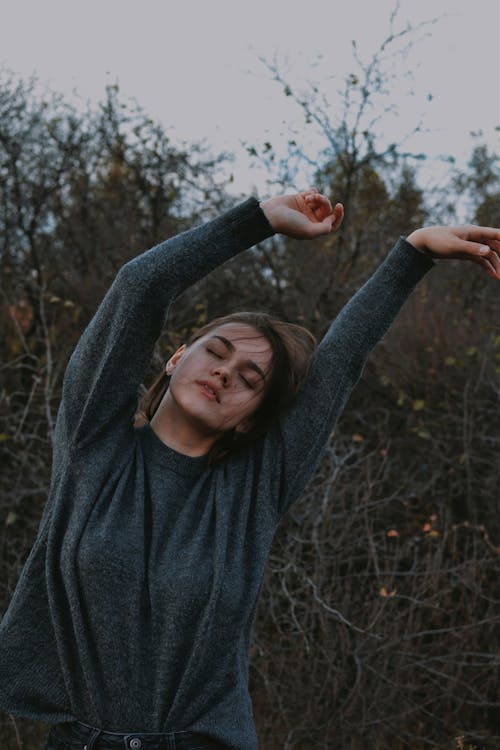 Young Woman with Eyes Closed and Arms Raised Outdoors 