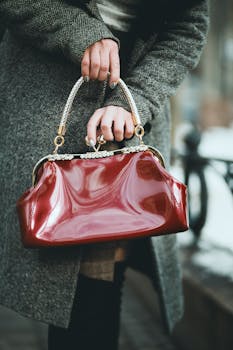 一位时尚的女士手持闪亮的红色皮革手袋，在户外优雅地展示着时尚风采