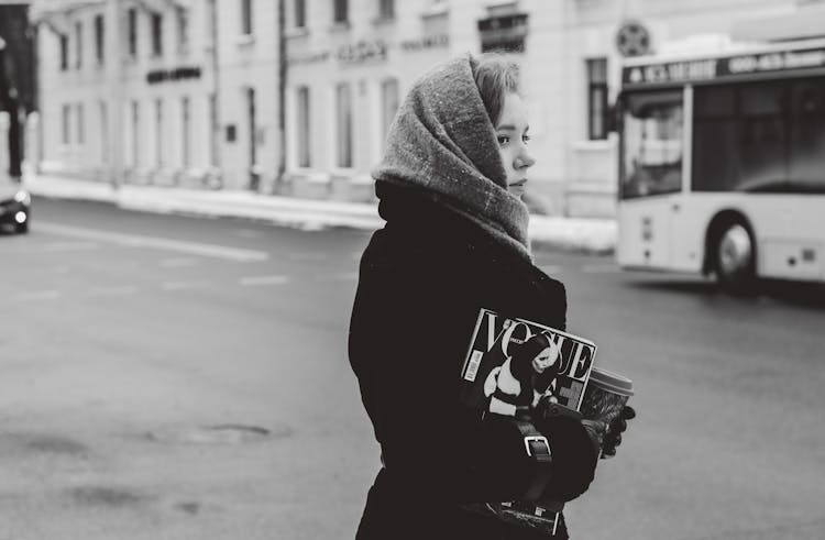 Woman In Warm Clothing On A City Street Holding A Magazine And Coffee