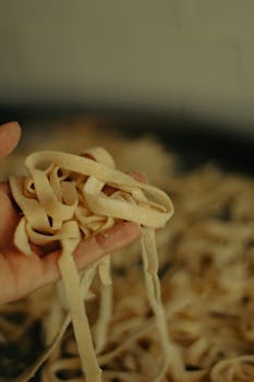 A hand holding freshly made raw fettuccine pasta, showcasing traditional Italian cuisine preparation.