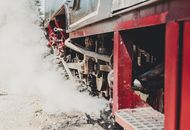 Detailed view of a vintage steam locomotive engine with steam and smoke outdoors.