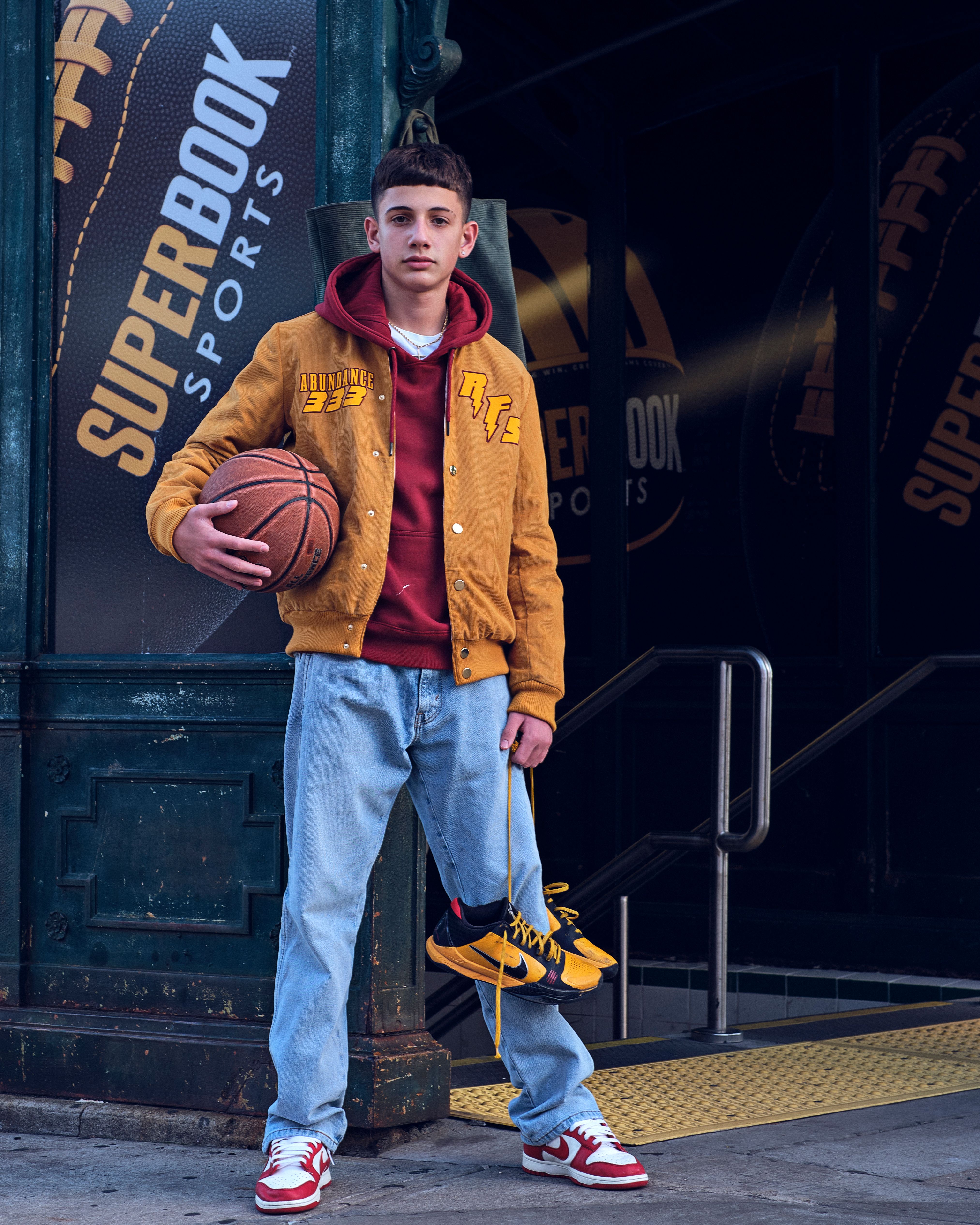 Young man in streetwear holding basketball on city street.