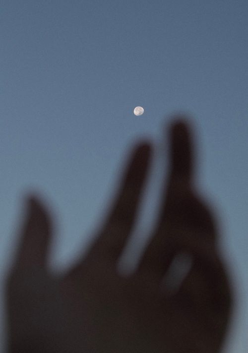 Free Silhouette of a hand reaching for the full moon against a night sky. Stock Photo