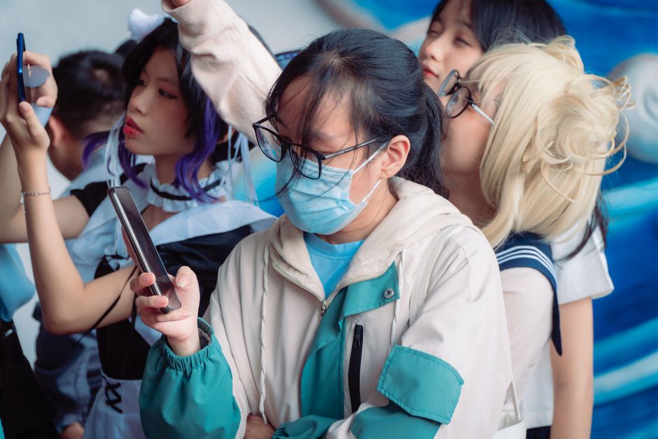 Group of young cosplayers using smartphones at an event, dressed in various costumes.