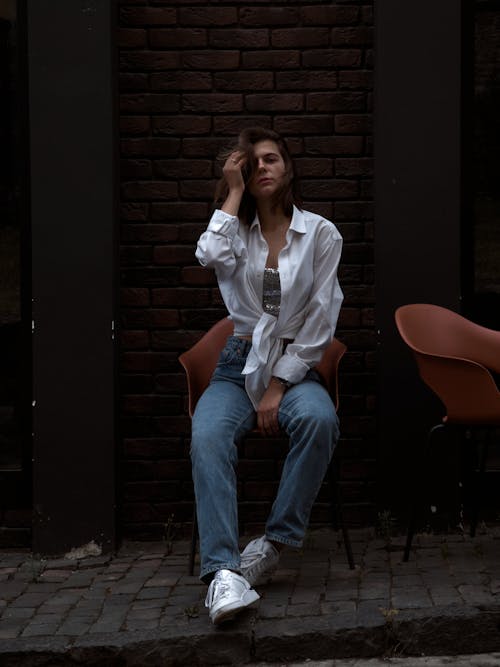 A Woman in a White Long Sleeved Shirt and Denim Pants Sitting on a Chair