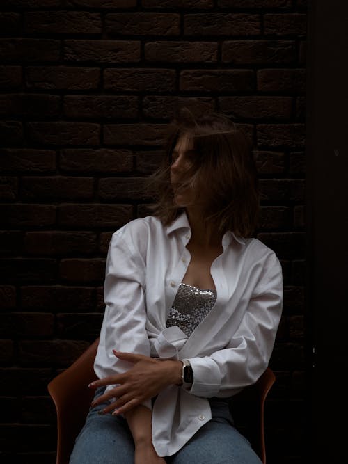 A Woman in White Long Sleeves Sitting near the Brick Wall 