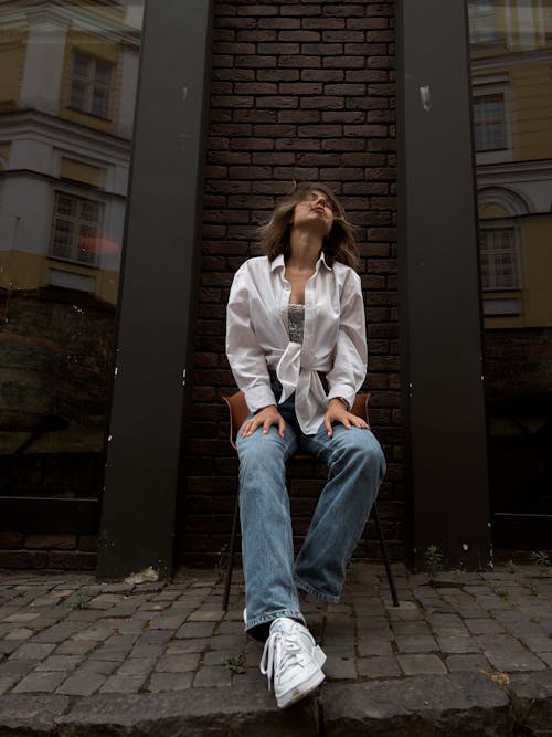 A Woman in a White Long Sleeved Shirt and Denim Pants Sitting on a Chair