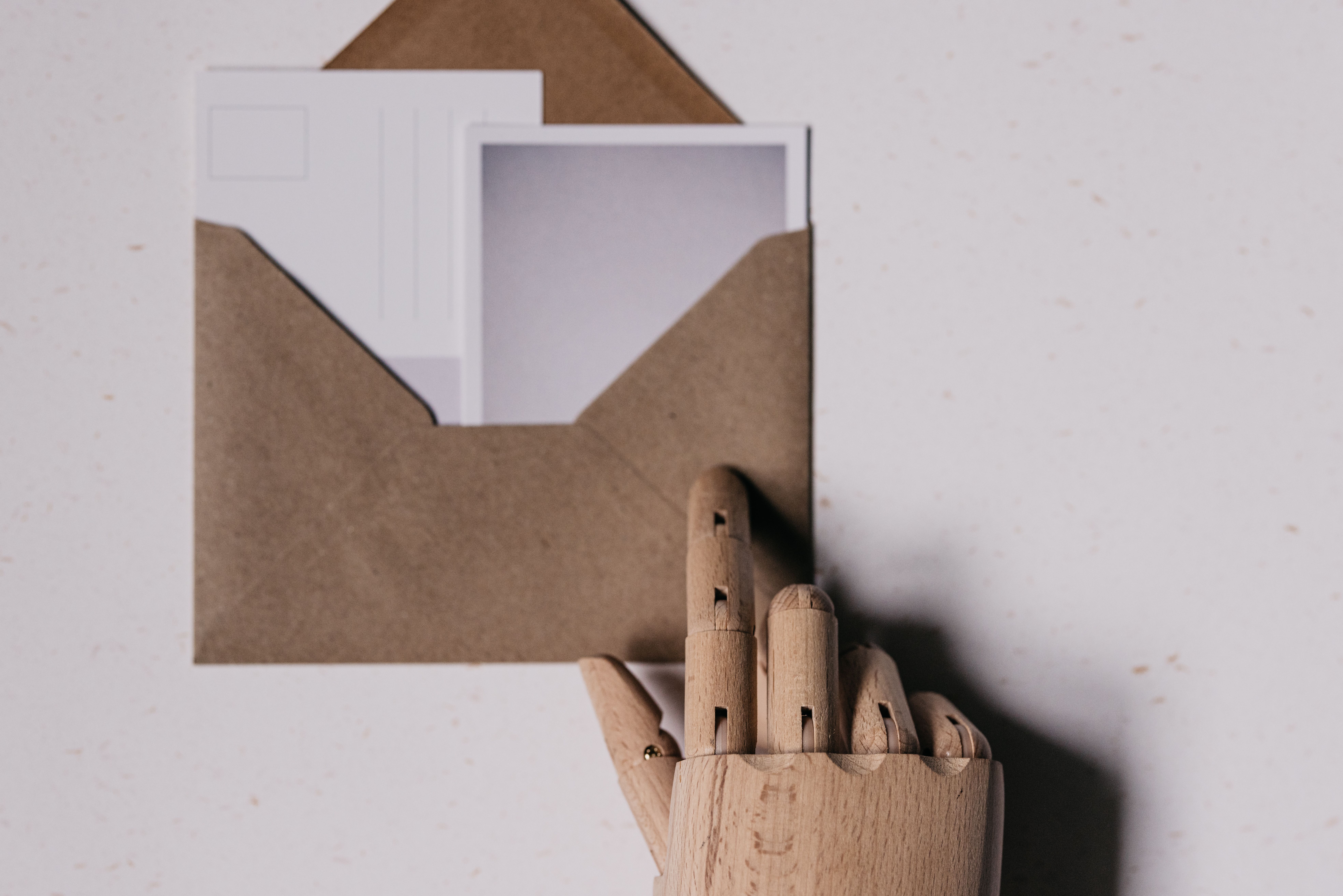 A wooden mannequin hand holds a brown envelope containing blank postcards.