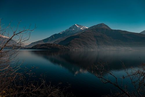 Free A tranquil mountain landscape with reflective lake and bare trees at twilight. Stock Photo