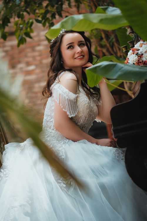 Free Beautiful bride in a white gown posing elegantly amidst lush greenery. Stock Photo