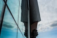 一座现代建筑的玻璃立面上，倒映出圆滑的建筑轮廓和多云的天空