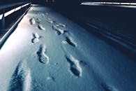 在黑暗的冬季道路上，脚印拖着新雪，在夜间照亮