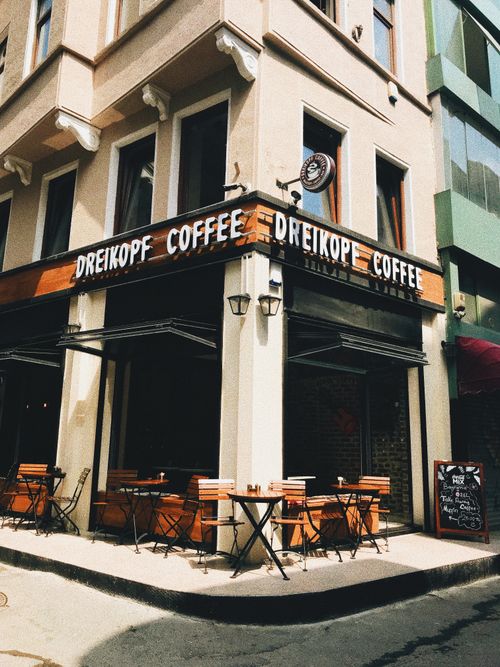 Free Charming corner café with wooden tables and chairs in a sunlit urban setting. Stock Photo