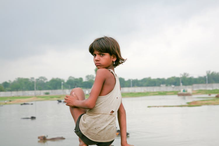 A Girl In Tank Top Sitting Near A Lake While Looking Afar