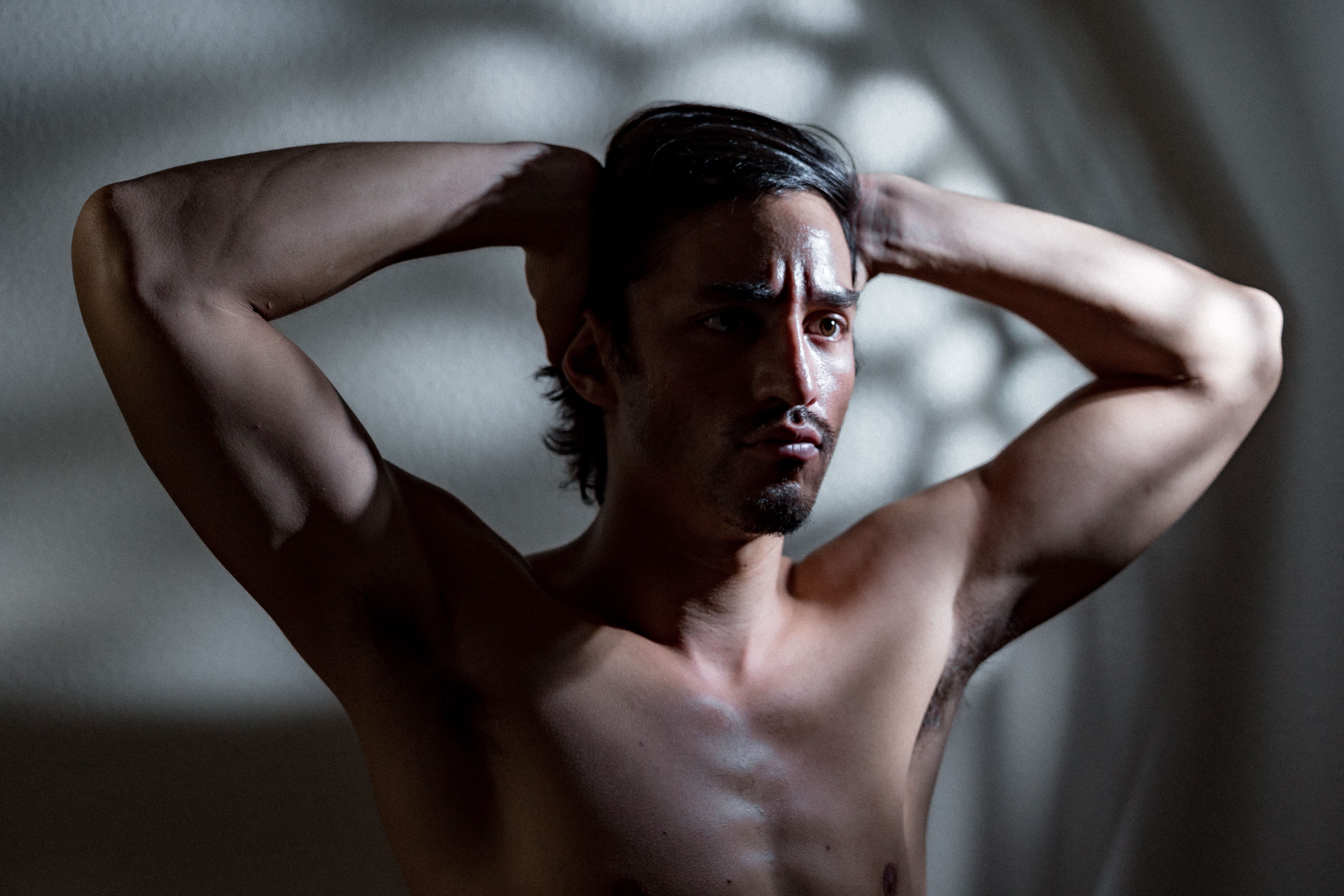 A shirtless man in dramatic light poses thoughtfully, showcasing physique and emotion.