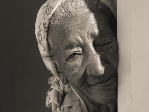 A Grayscale of an Elderly Woman Leaning on a Wall