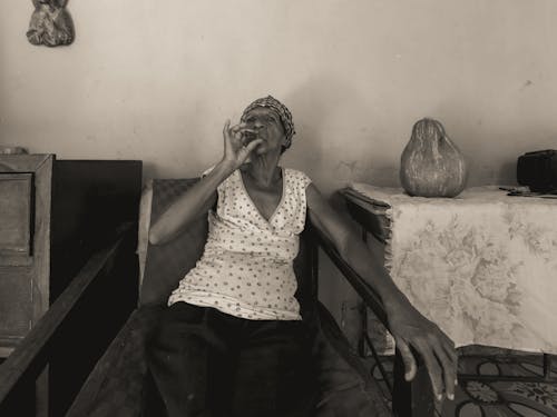 An Elderly Woman Wearing Headscarf Sitting on a Chair while Smoking Tobacco 