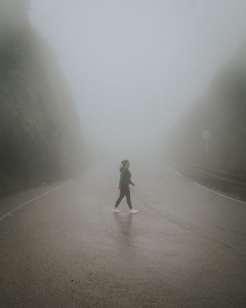 Free A solitary person walks on a foggy road surrounded by dense mist, evoking a mysterious atmosphere. Stock Photo
