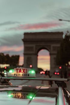 Taxi sign against a sunset sky and Arc de Triomphe in Paris, capturing urban evening vibe.