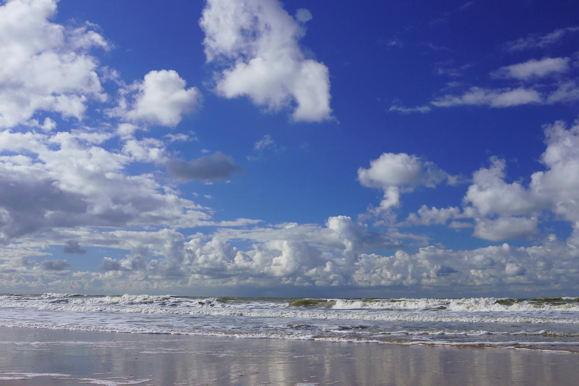 Beautiful beach with waves and clouds in Oostende, Belgium under a blue sky.