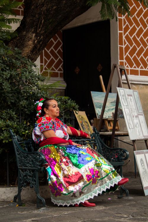 Free Woman in traditional dress sitting on a bench at an outdoor art market, vibrant cultural scene. Stock Photo
