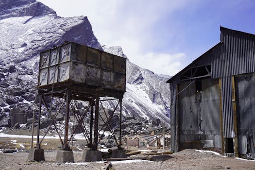 An abandoned industrial site amidst the snowy mountains of Argentina, showcasing decay and rustic architecture.
