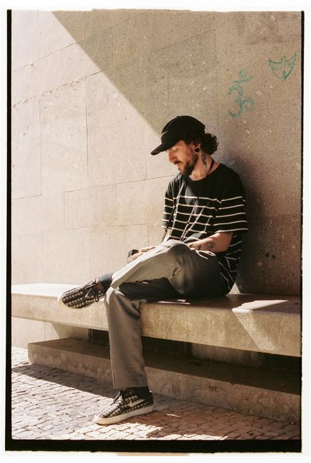 Young man with tattoos sitting on a concrete bench, reading outdoors.