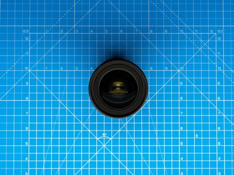 A camera lens placed on a blue grid cutting mat, capturing a top view shot.