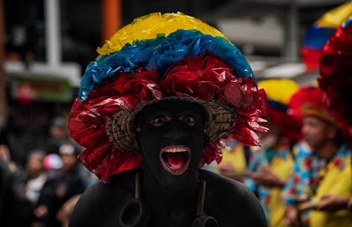 Man with Black Face and Body Paint Wearing a Multicolored Headdress at a Festivity