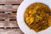 Close-up of spicy Indian curry with vegetables served in a white plate on a rustic wooden table.