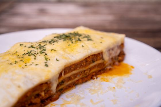 Thick slice of beef lasagna with melted golden mozzarella and parsley on a white plate