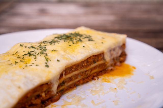 Close-up shot of a cheesy homemade lasagna slice on a plate, highlighting its layers and garnish.