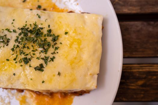 Close-up of a delicious cheesy lasagna slice topped with fresh herbs on a plate.