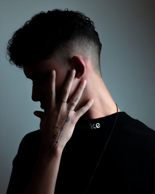 Moody portrait of a man showing his tattooed hand and stylish haircut, in a dark ambiance.