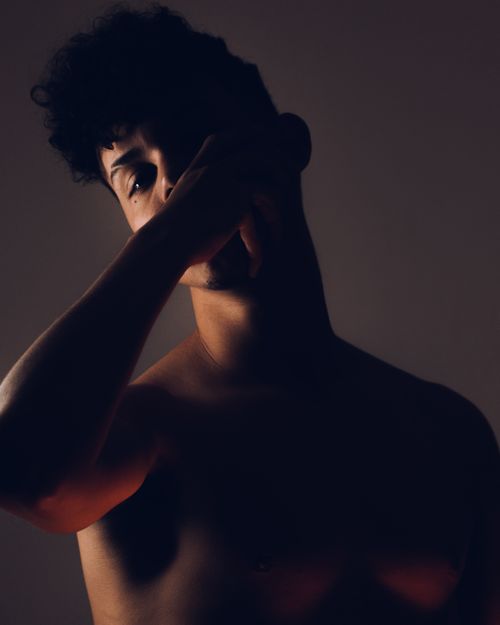 Free A thoughtful, moody portrait of a topless man with short hair, partially covering his face. Stock Photo
