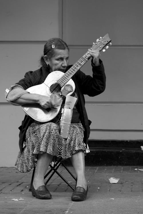 Grayscale Photo of an Elderly Woman Playing an Acoustic Guitar