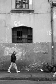 Black and white photo of a woman walking past a graffiti-covered wall in an urban setting.