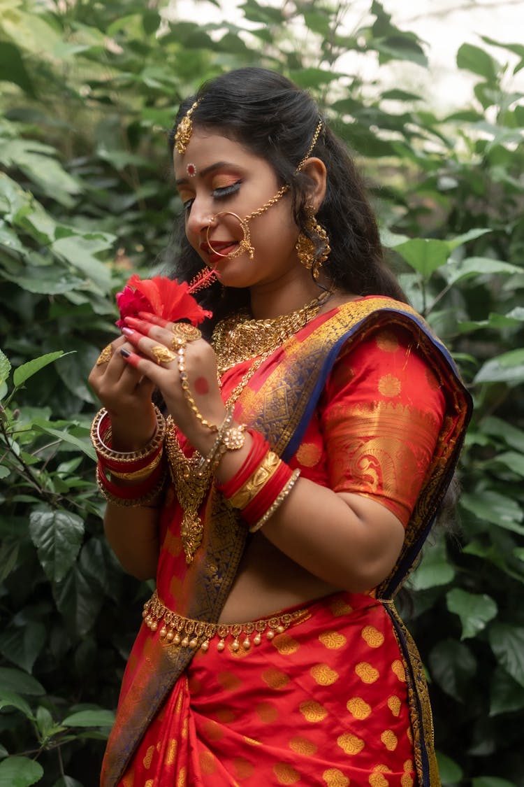 A Woman In A Red And Gold Sari Dress Holding Red Flower