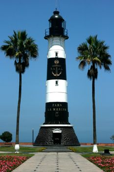 Beautiful view of La Marina Lighthouse surrounded by palm trees and vibrant gardens in Miraflores, Lima.