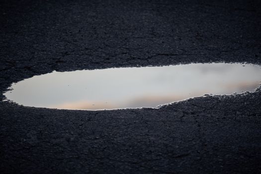 A close-up view of a reflective puddle on rough asphalt, capturing the tranquil ambience.