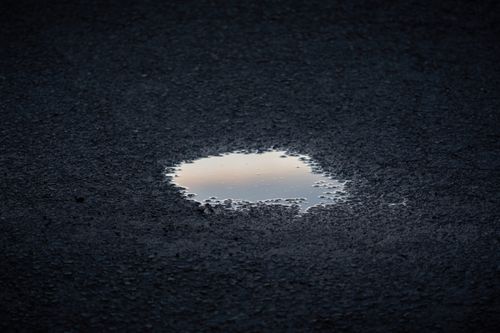 Free A tranquil puddle reflecting the sky on a textured asphalt road. Stock Photo