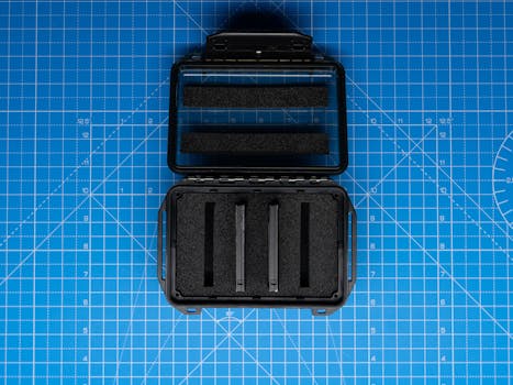 Top view of black protective equipment case on a blue cutting mat with grid lines.