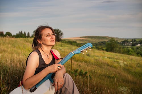 A Woman Holding an Acoustic Guitar while Sitting on a Grass Field