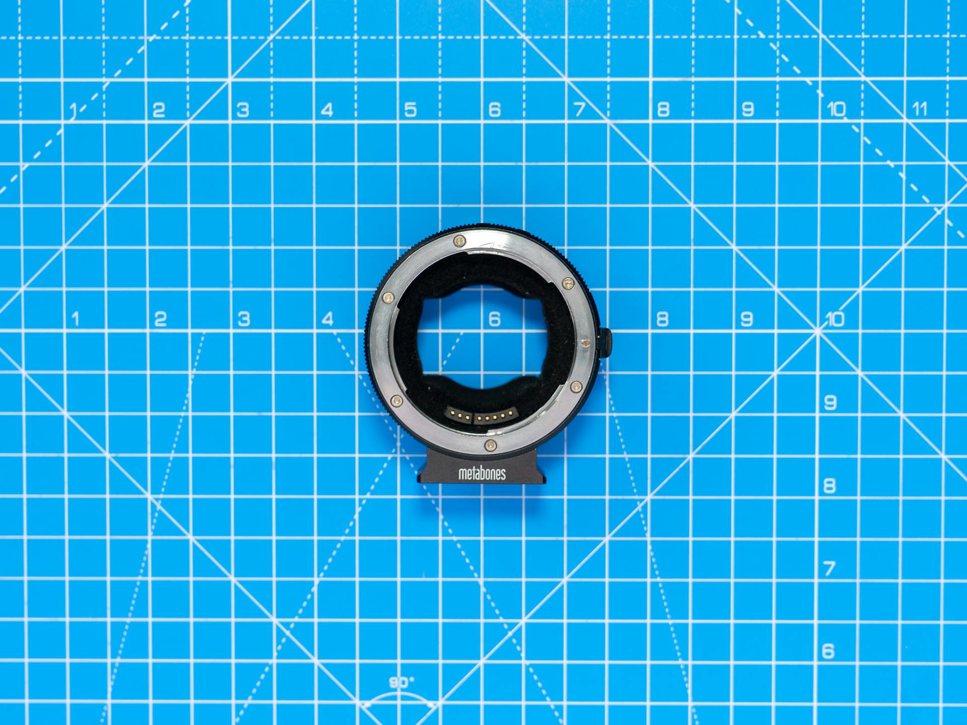 Close-up of a Metabones lens adapter on a blue grid background, ideal for product photography.