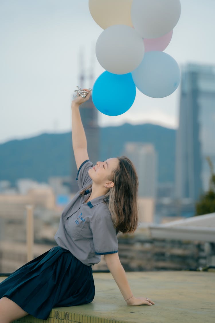 A Woman In Gray Polo Holding Balloons While Smiling 