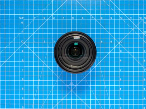 A detailed close-up of a camera lens placed on a blue grid pattern surface.