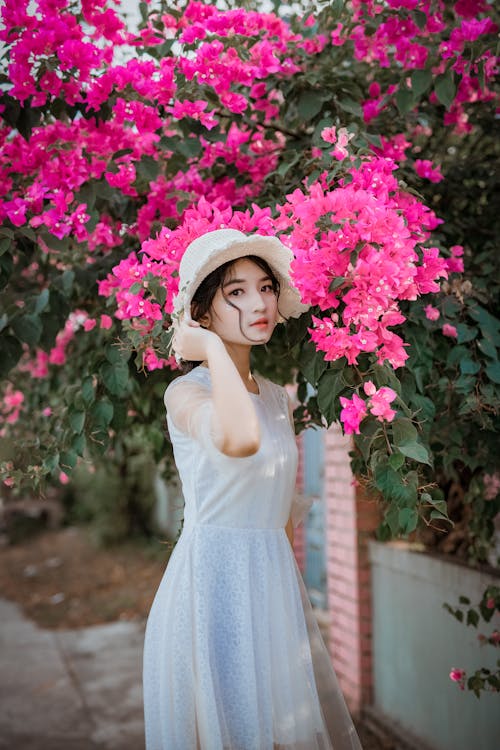 ピンクのブーゲンビリアの花の前に立っている間彼女の帽子を保持している女性