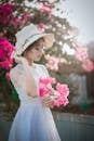 Woman Wearing Sun Hat and White Dress Holding Pink Bougainvilleas