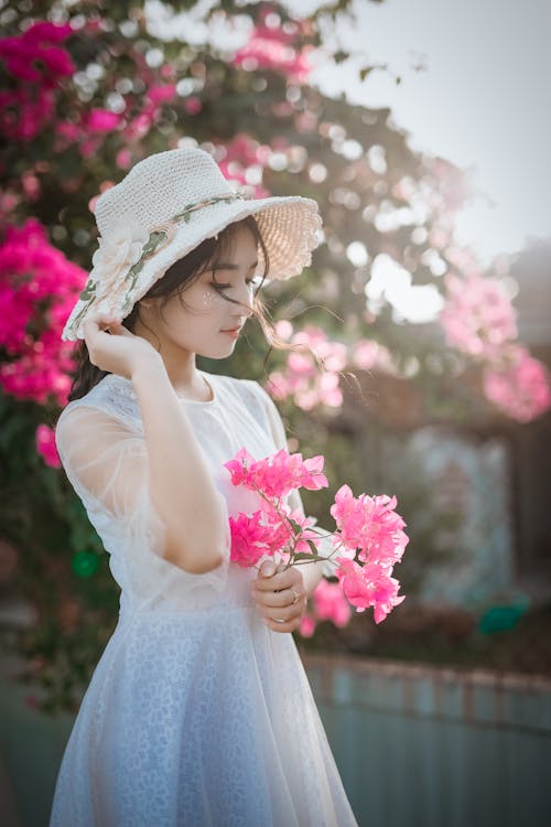 Woman Wearing Sun Hat and White Dress Holding Pink Bougainvilleas